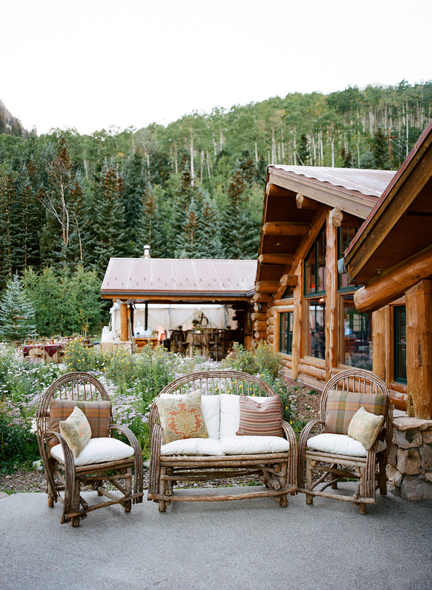 Summer evening on the Pine Creek Cookhouse patio - willow lounge chairs, wildflowers, and the log cabin beyond.